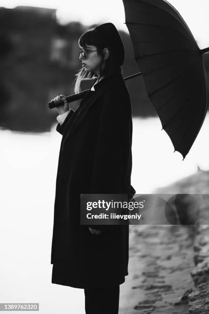 black white photography. redhead girl in black clothes outdoors. gothic style. asian fashion model in dark coat with umbrella on nature. bw photo. stylish outfit. subculture. monochrome. desaturated - gothic style stockfoto's en -beelden