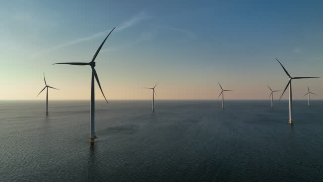 Wind turbines offshore producing electricity during sunset