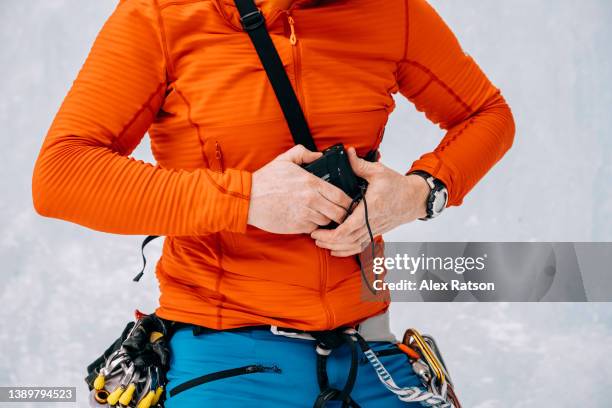 close up of an ice climber putting on an avalanche transceiver beacon while at the base of a frozen waterfall - red beacon stock pictures, royalty-free photos & images