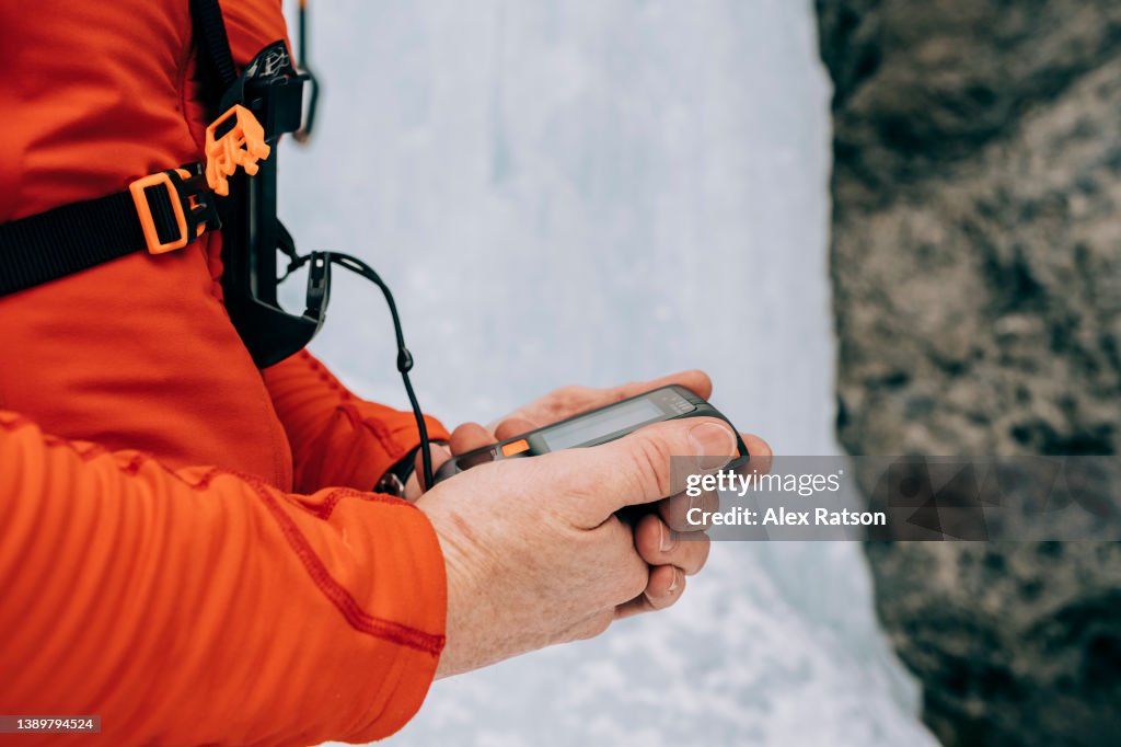 Close up of an ice climber testing an avalanche transceiver beacon before climbing a frozen waterfall