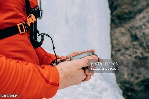 close up of an ice climber testing an avalanche transceiver beacon before climbing a frozen waterfall - red beacon stock pictures, royalty-free photos & images