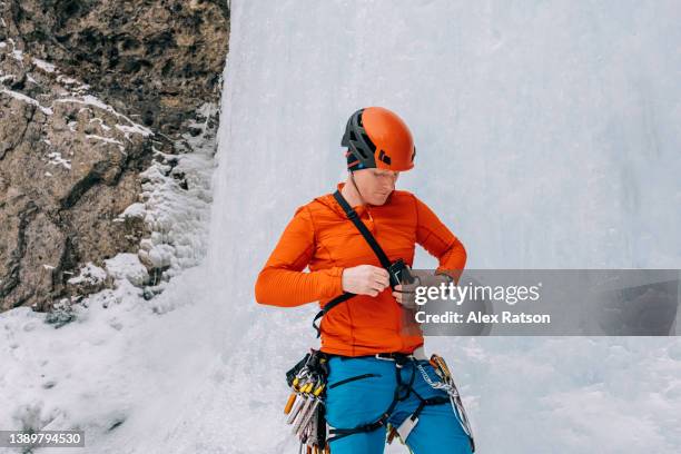 an ice climber puts on an avalanche transceiver beacon while at the base of a frozen waterfall - transceiver stock pictures, royalty-free photos & images