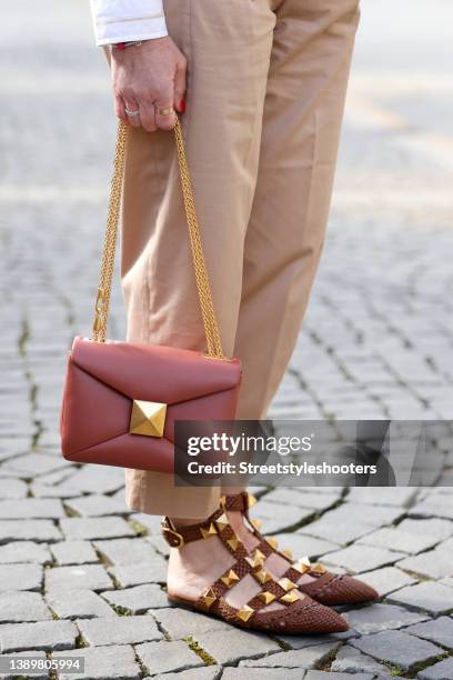 Influencer Simone Adams wearing brown flat sandals with gold studs by Valentino and a rust colored bag with gold details by Valentino during a street...