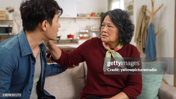 asiatische senior-oma sitzt mit leerem gesicht auf der couch und verwechselt ihren enkel mit ihrem mann zu hause. falsches gedächtnis im alzheimer-konzept - memory loss stock-fotos und bilder