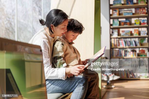 mother and son reading book by the window - library kids stock pictures, royalty-free photos & images