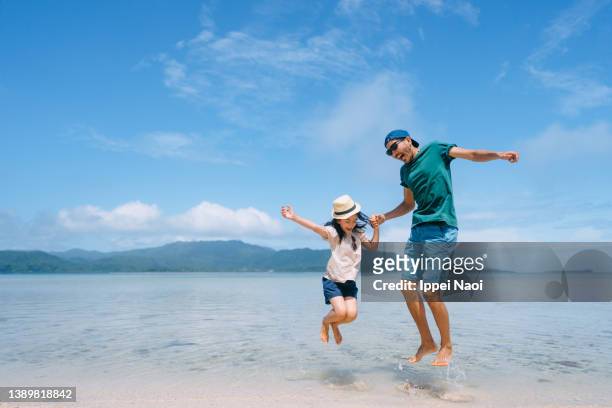 father and young daughter jumping on beach - beach holiday stock pictures, royalty-free photos & images