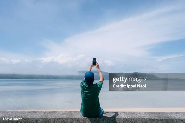 man taking photo of island with smartphone - okinawa japan stockfoto's en -beelden