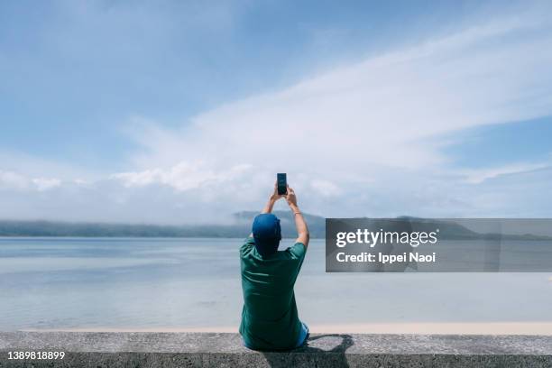 man taking photo of island with smartphone - man taking photos stock pictures, royalty-free photos & images