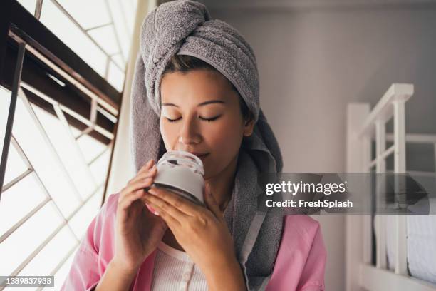 ritratto di una bella donna asiatica che sente l'odore della crema da giorno che usa come parte della routine di cura del viso - coconut oil foto e immagini stock