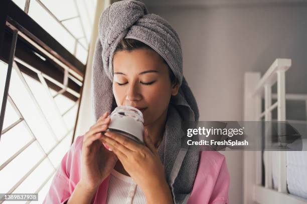 portrait of a beautiful asian woman smelling the day cream she uses as part of face care routine - haarbehandeling stockfoto's en -beelden
