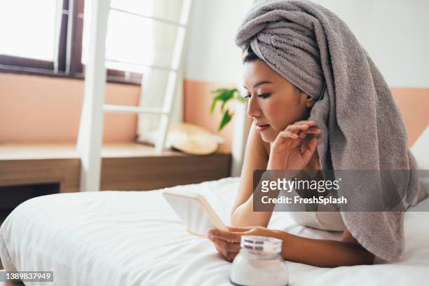 ベッドに横たわり、手鏡で顔を見る美しいアジア人女性 - hand in hair ストックフォトと画像