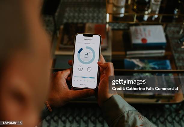 a man controls a thermostat with an app on his mobile device - engenheiro de aquecimento - fotografias e filmes do acervo