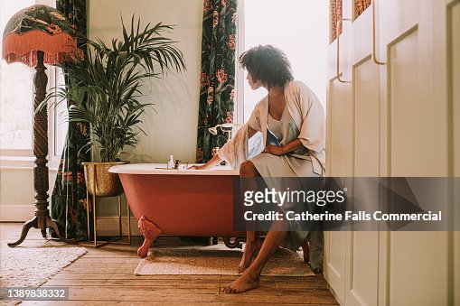 Dreamy scene of a beautiful woman perching on the side of a roll top bathtub in a luxurious room