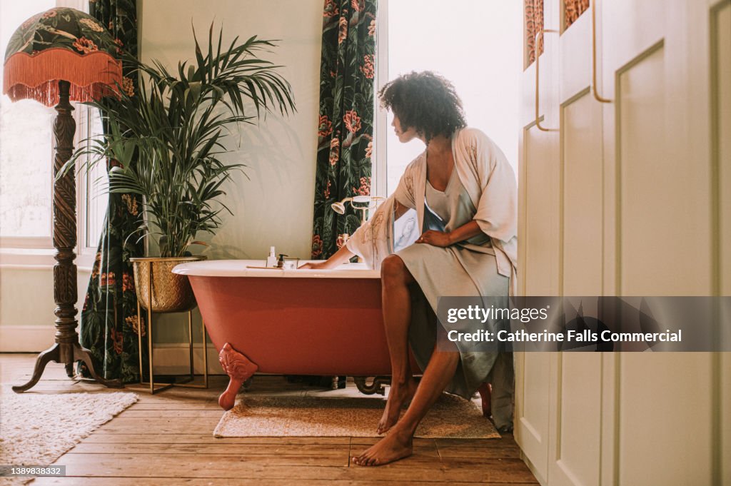 Dreamy scene of a beautiful woman perching on the side of a roll top bathtub in a luxurious room