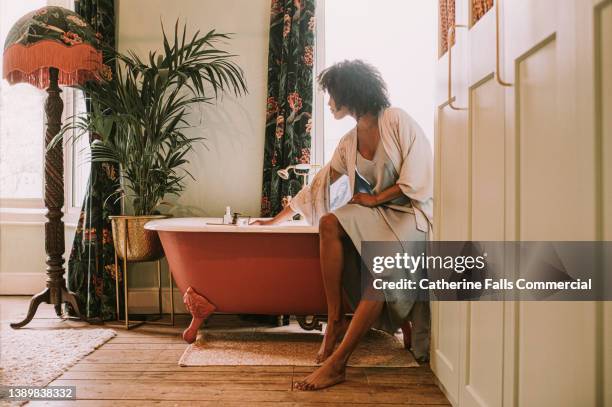 dreamy scene of a beautiful woman perching on the side of a roll top bathtub in a luxurious room - relaxado imagens e fotografias de stock