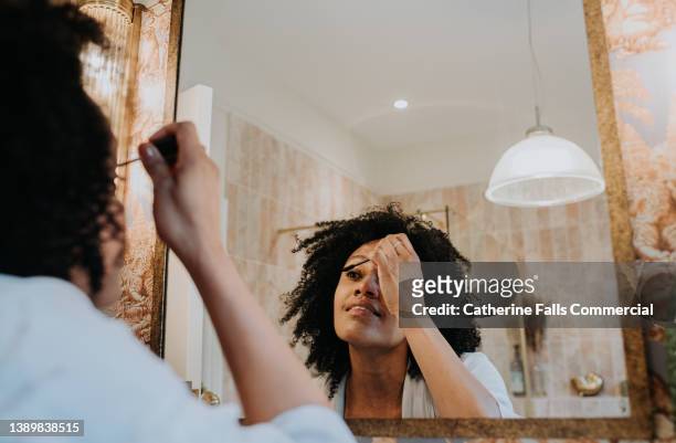 a woman applies mascara in a bathroom mirror - パウダールーム　女性 ストックフォトと画像
