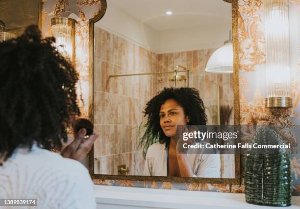 a woman applies foundation in a bathroom mirror - exfoliation face stock pictures, royalty-free photos & images