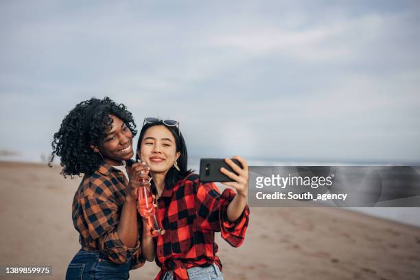 two friends walking the beach drinking soda and taking a selfie - asian female friends drinking soda outdoor stockfoto's en -beelden