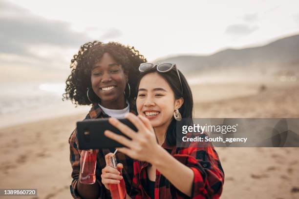 two friends walking the beach drinking soda and taking a selfie - asian female friends drinking soda outdoor stockfoto's en -beelden