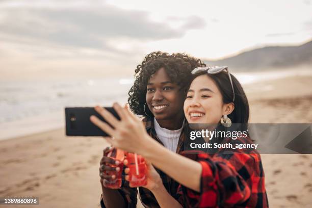 two friends walking the beach drinking soda and taking a selfie - asian female friends drinking soda outdoor stock pictures, royalty-free photos & images