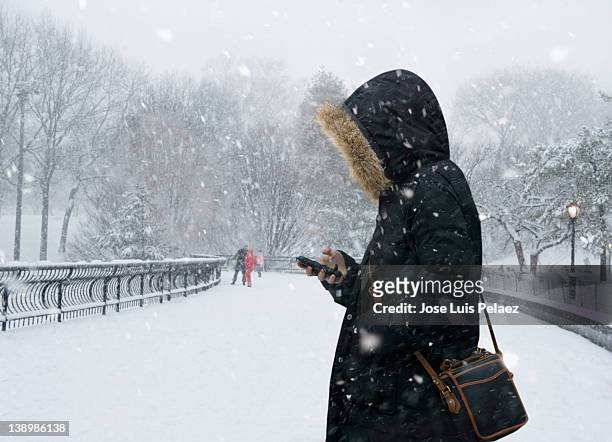 young woman checking phone in snow - winter_storm stock pictures, royalty-free photos & images