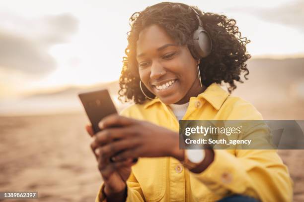 jovem negra ouvindo música em fones de ouvido sem fio na praia - beautiful south african women - fotografias e filmes do acervo