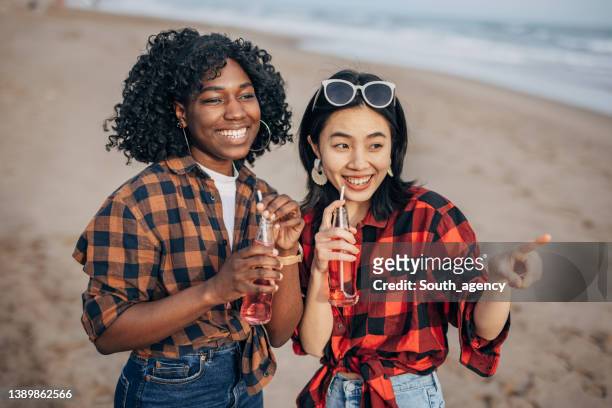 two hipster friends walking on the beach and drinking soda - asian female friends drinking soda outdoor stockfoto's en -beelden