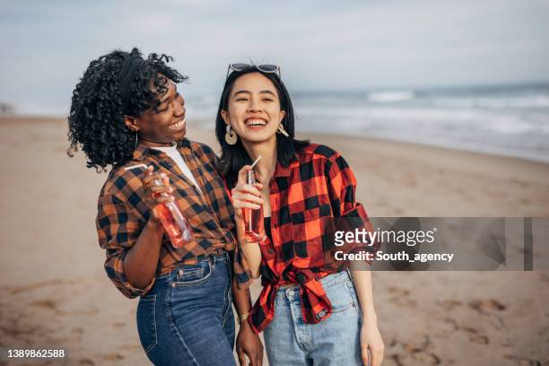 two hipster friends walking on the beach and drinking soda - asian female friends drinking soda outdoor stockfoto's en -beelden