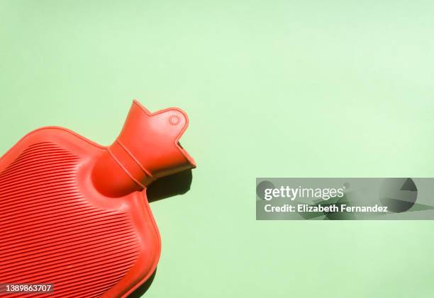 red hot water bottle on green background - heat illness stock pictures, royalty-free photos & images