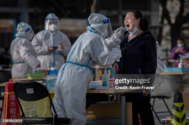 Health worker wears protective gear as she gives a nucleic acid test to detect COVID-19 on a local resident at a mass testing site after new cases...