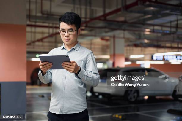 a male parking lot keeper using an ipad while standing in an underground parking garage - valet stock-fotos und bilder