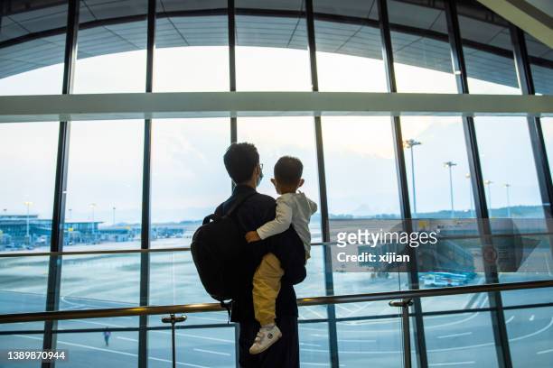 man with his son waiting for the flight at window of the airport - leaving airport stock pictures, royalty-free photos & images