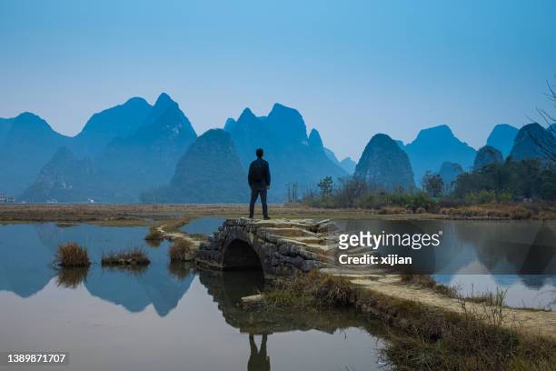 male tourist with a backpack goes on the stone bridge ,guilin,china - yangshuo imagens e fotografias de stock