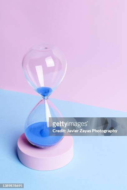 blue colored sand hourglass on blue and pink background - measuring potential business stock pictures, royalty-free photos & images