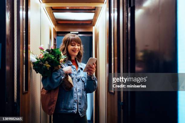 donna sorridente che usa il suo telefono cellulare nell'ascensore - lift foto e immagini stock