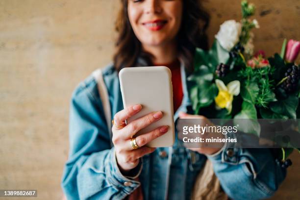 una donna anonima che tiene fiori e usa un telefono cellulare - dating app foto e immagini stock