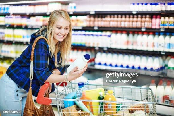 une belle jeune femme admire une bouteille de lait alors qu’elle fait ses courses dans un supermarché - bouteille de lait photos et images de collection