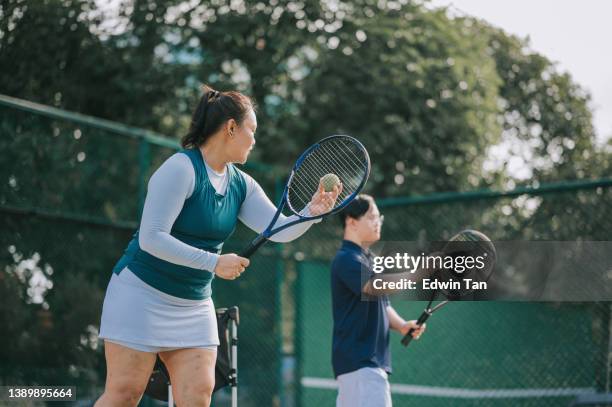 asian chinese down syndrome man learning from female coach trainer playing tennis during weekend morning - racquet sport stock pictures, royalty-free photos & images