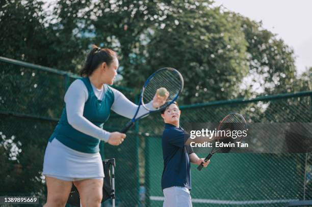 hombre asiático chino con síndrome de down aprendiendo de entrenadora entrenadora que juega al tenis durante la mañana del fin de semana - disabilitycollection fotografías e imágenes de stock