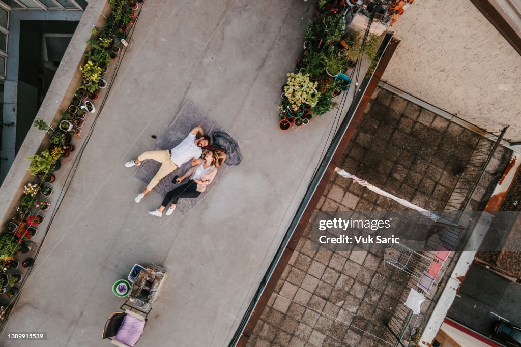 Drone point of view of a couple laying on a blanket on roof garden and smiling
