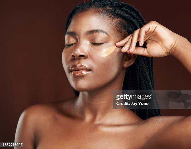 studio shot of an attractive young woman applying makeup against a brown background - make up foundation stock pictures, royalty-free photos & images