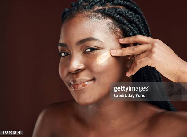 studio shot of an attractive young woman applying makeup against a brown background - applicera bildbanksfoton och bilder