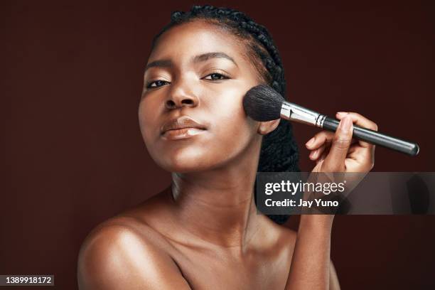 studio shot of an attractive young woman applying makeup against a brown background - sminkborste bildbanksfoton och bilder