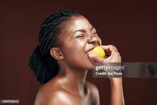 foto de estudio de una atractiva joven comiendo un limón sobre un fondo marrón - sabor amargo fotografías e imágenes de stock