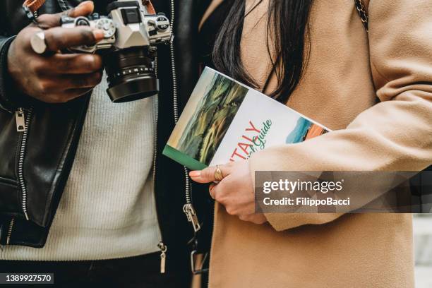 detail of a couple of young adults holding a camera and a guidebook - guidebook stock pictures, royalty-free photos & images