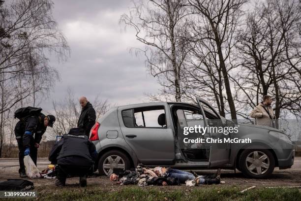 Police officers search a car next to the a woman's body that was found in a car shot by Russian forces on a roadside on April 6, 2022 in Bucha,...