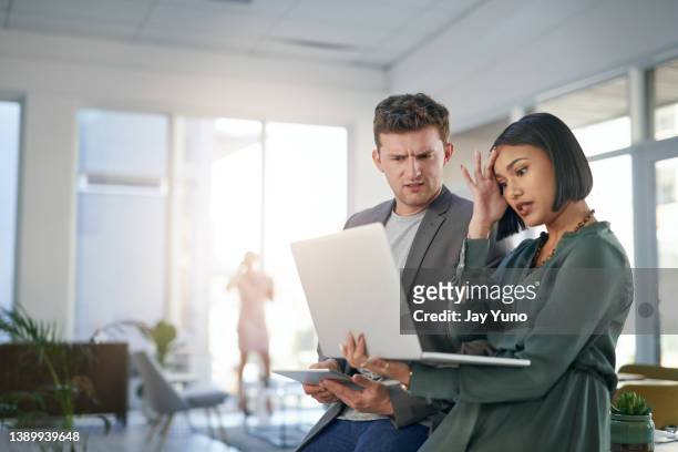 scatto di un giovane uomo d'affari e donna d'affari che sembra stressato mentre usa un laptop durante una riunione in un ufficio moderno - mistake foto e immagini stock