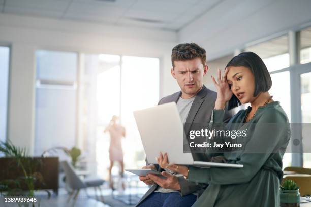 shot of a young businessman and businesswoman looking stressed out while using a laptop during a meeting in a modern office - laptop desperate professional stockfoto's en -beelden