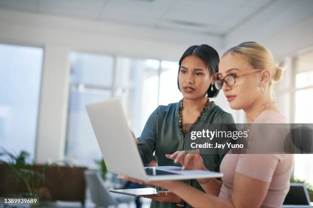 shot of two young businesswomen using a laptop during a meeting in a modern office - co workers looking at computer stockfoto's en -beelden