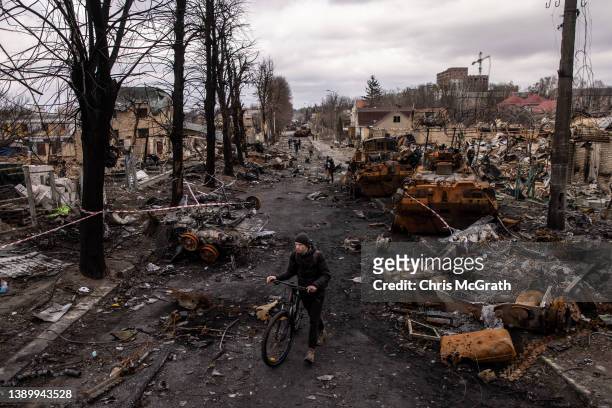 Man pushes his bike through debris and destroyed Russian military vehicles on a street on April 06, 2022 in Bucha, Ukraine. The Ukrainian government...